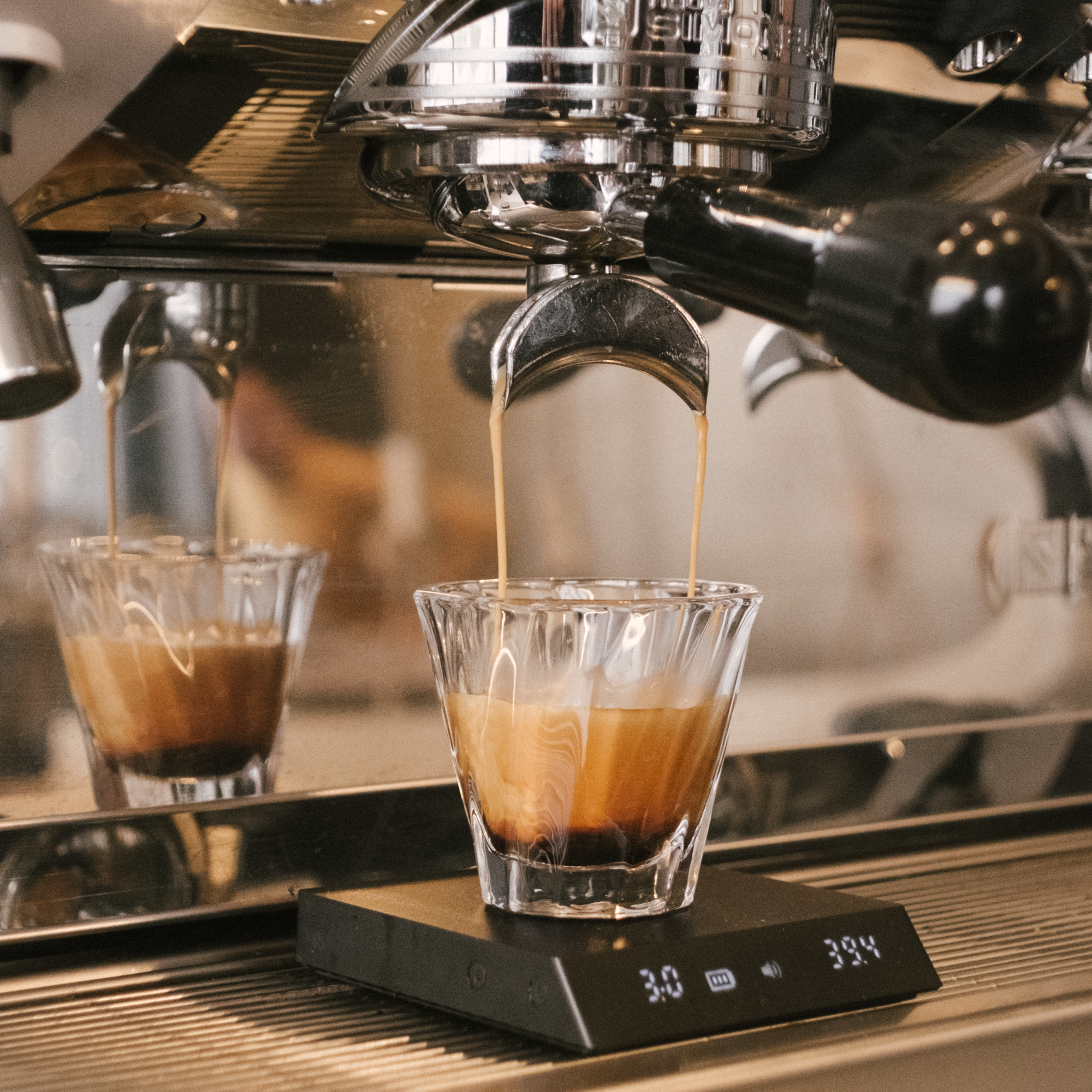 Extracting an espresso shot with rich crema dripping into a glass shot glass placed on a scale.